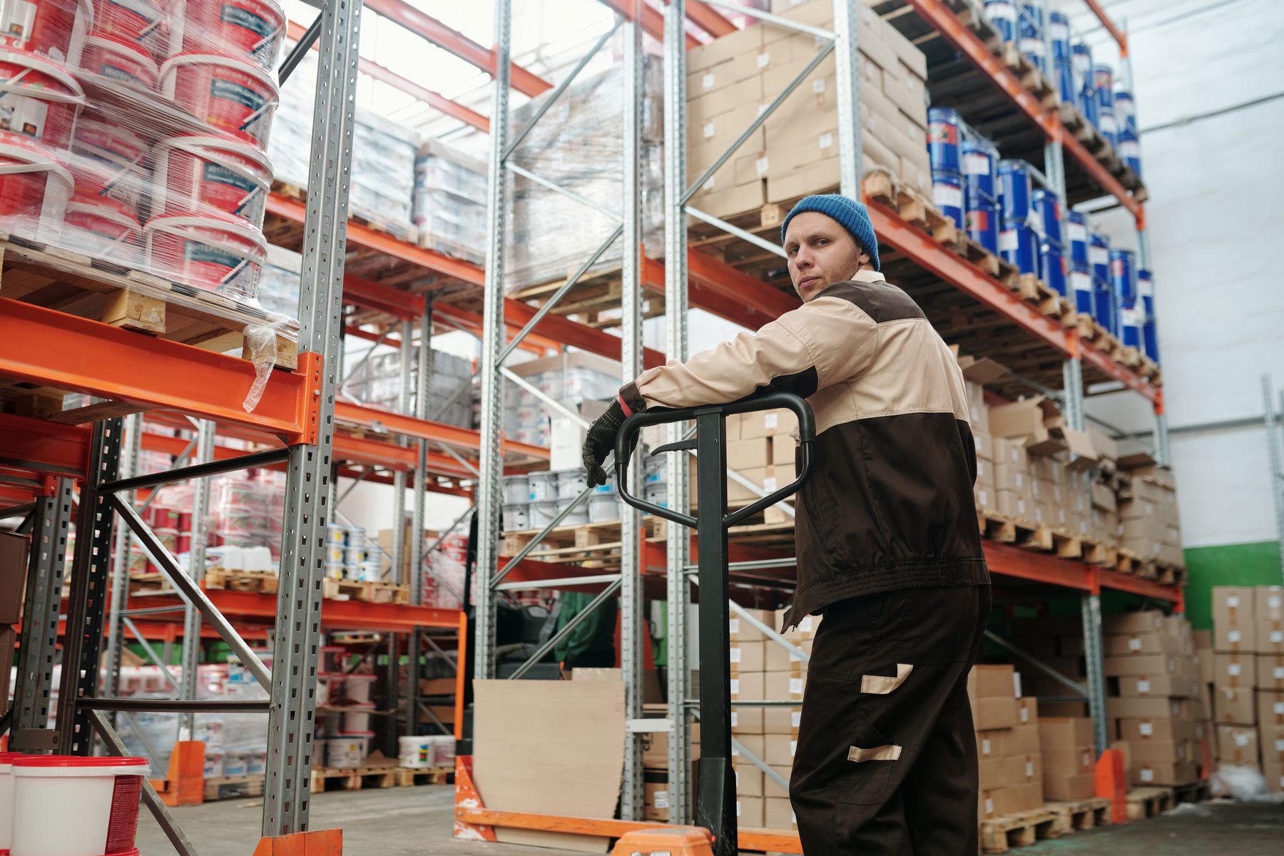 Warehouse worker operating a pallet jack between stocked racks